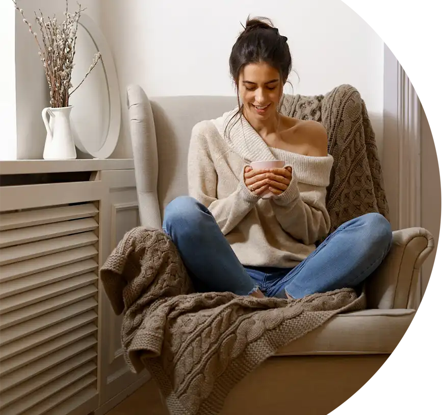 Mieterin sitzt entspannt mit Heißgetränk im warmen Wohnzimmer – wohlige Atmosphäre dank effizientem Heizen und gerechter CO₂-Kostenaufteilung.